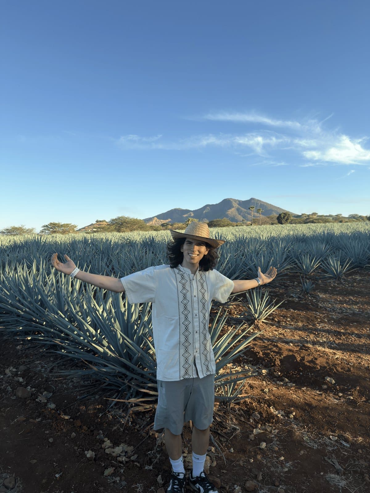 Santiago Billeci standing in an agave field with his arms out